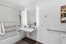 Wall-mounted floating vanity with integrated sink, rectangular illuminated mirror, white subway-tiled shower surround, matte black plumbing fixtures, 