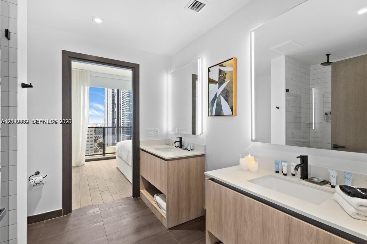 Dual wood-finish floating vanities featuring stone-style countertops, rectangular undermount sinks, matte black fixtures, and integrated LED-backlit m