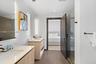 Dual vanity with light wood-finish cabinetry, solid surface countertops, integrated LED-lit mirrors, and glass-enclosed shower with subway tile