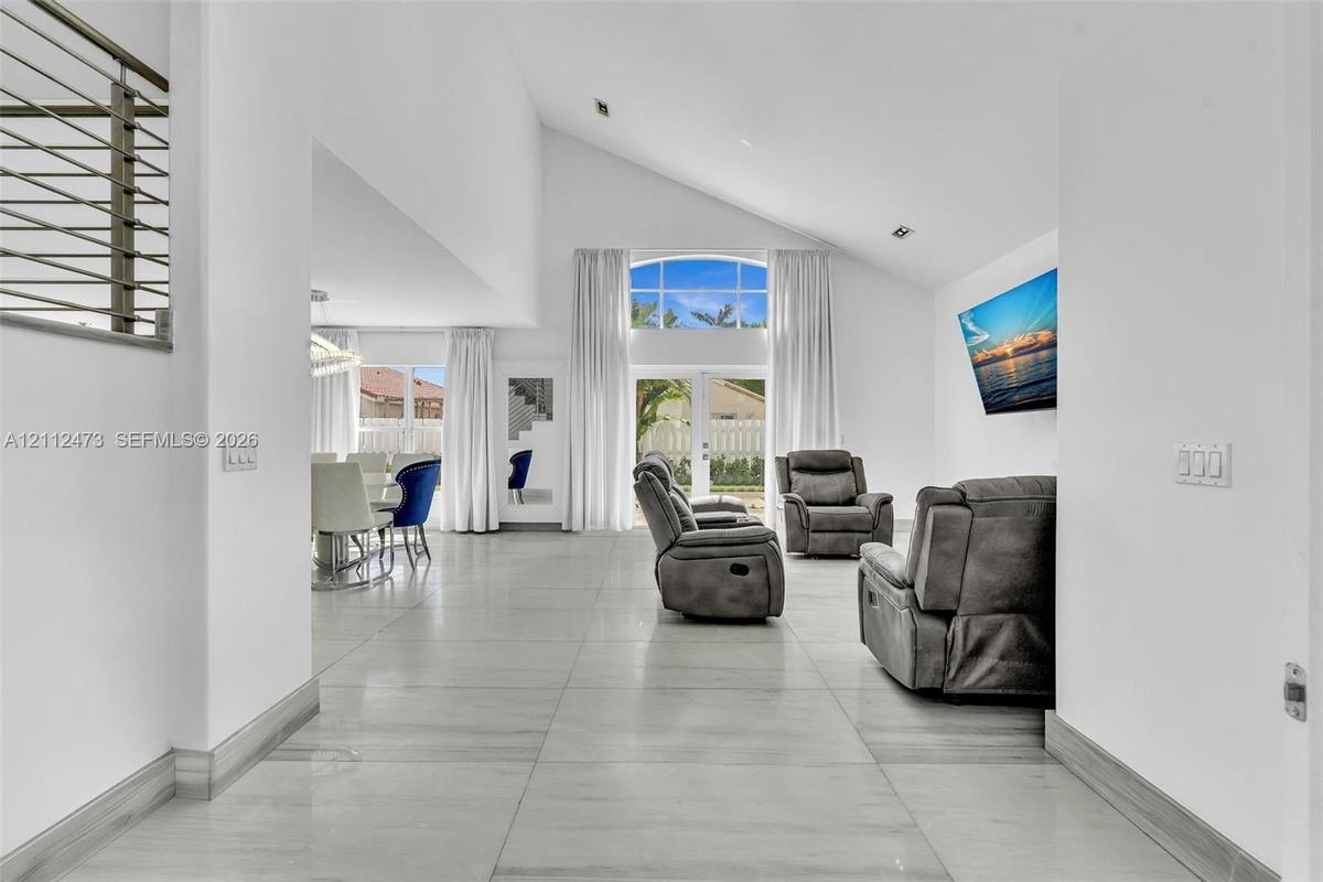 Vaulted ceilings, large-format tile flooring, double-door glass entrance with arched transom window, and metal cable railing