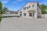 Stucco exterior featuring a tile-accented roof, expansive concrete patio, bay window, and white vinyl privacy fencing