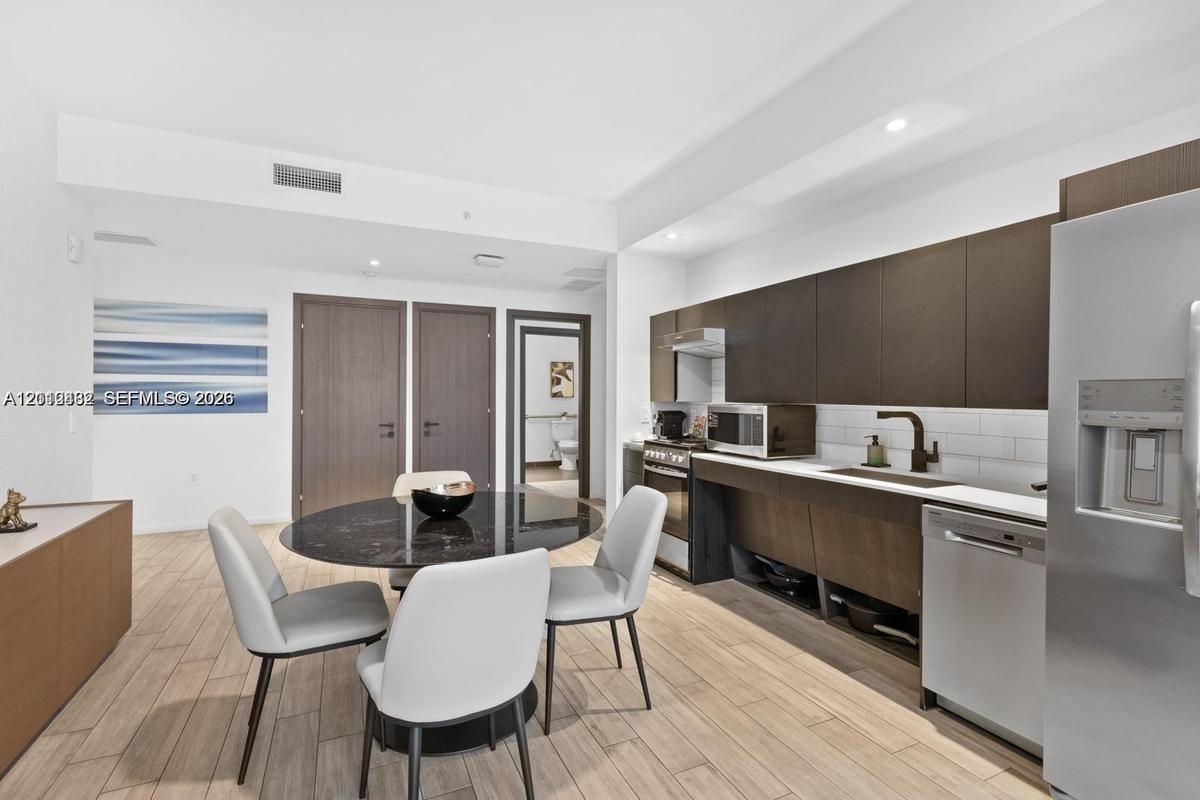 Contemporary kitchen featuring flat-panel cabinetry, stainless steel appliances, subway tile backsplash, recessed lighting, and wood-finish flooring