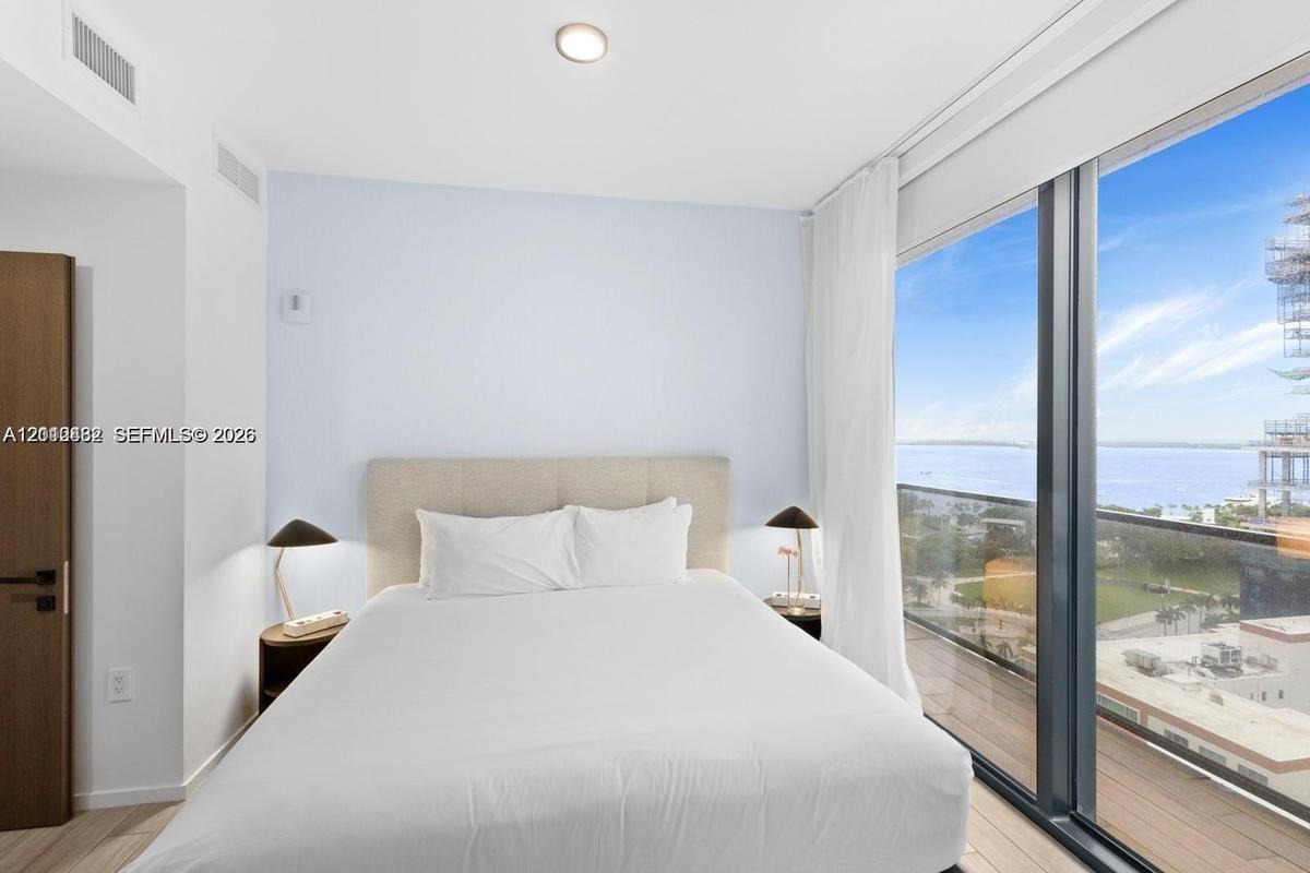 Floor-to-ceiling windows, wood-finish flooring, and access to a private balcony with water scenery