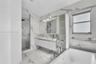 Bathroom featuring floor-to-ceiling large-format stone-patterned wall tile, white floating double vanity with integrated sinks, glass-enclosed walk-in