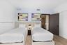 Neutral-toned upholstered headboard with integrated nightstand, wood-finish flooring, and dark-finished solid core swing door