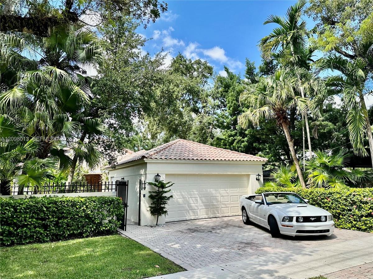 garage featuring a tile roof, stucco exterior, paver driveway, and black metal perimeter fencing surrounded by mature landscaping