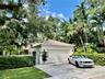 garage featuring a tile roof, stucco exterior, paver driveway, and black metal perimeter fencing surrounded by mature landscaping