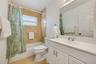 Bathroom featuring a white vanity with an integrated basin, large wall-mounted mirror, tub with natural stone wall