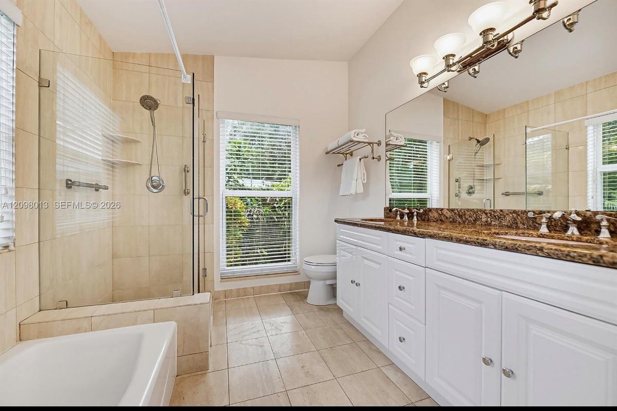 Bathroom featuring a double-sink vanity with stone countertop, walk-in glass-enclosed shower, separate tub tub