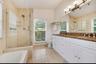 Bathroom featuring a double-sink vanity with stone countertop, walk-in glass-enclosed shower, separate tub tub