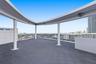 Rooftop terrace featuring dark modular interlocking flooring, a curved architectural canopy supported by cylindrical columns, and metal perimeter rail