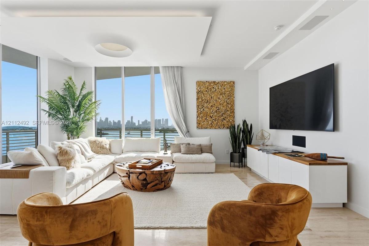 Living area featuring floor-to-ceiling windows, custom recessed tray ceiling with integrated lighting, polished stone flooring, and built-in low-profi