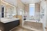 Bathroom featuring a wall-mounted floating vanity with integrated rectangular sink, large-format tiled wall surfacing, glass-enclosed shower and tub c