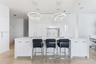 Modern kitchen featuring high-gloss cabinetry, a central island with a solid-surface countertop, dual contemporary ring pendant light fixtures, and st
