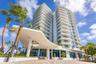 High-rise residential building featuring a sculpted architectural porte-cochère, stacked private balconies, floor-to-ceiling windows, and paved motor 