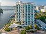 High-rise waterfront building featuring floor-to-ceiling glass windows, private balconies, a porte-cochère entryway, and tropical landscaping