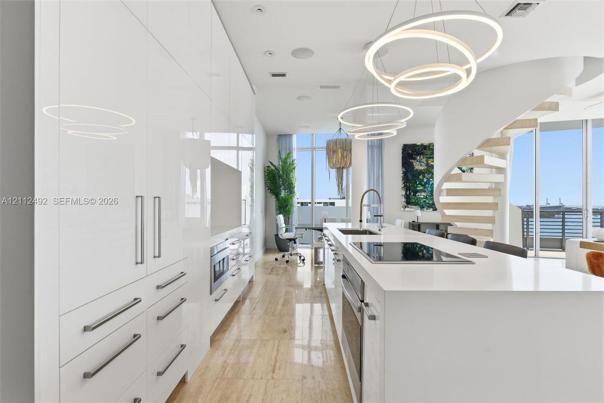 High-gloss cabinetry, stone-surfaced kitchen island, integrated stainless steel appliances, circular pendant lighting, and a sculptural spiral stairca