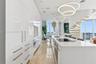 High-gloss cabinetry, stone-surfaced kitchen island, integrated stainless steel appliances, circular pendant lighting, and a sculptural spiral stairca