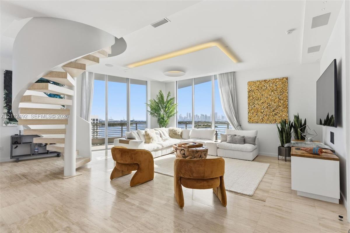Open-concept living space featuring a sculptural spiral staircase with wood-tread steps, polished stone flooring, recessed ceiling lighting, and floor