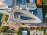 Aerial perspective of a multi-level structure featuring a distinctive triangular roofline, a circular driveway, integrated hardscaping, and immediate 