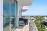 Covered balcony featuring full-height glass sliding doors, concrete flooring, and metal railings with coastal city scenery