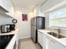 Kitchen featuring white flat-panel cabinetry, light-toned solid surface countertops, stainless steel refrigerator, undermount sink with gooseneck fauc