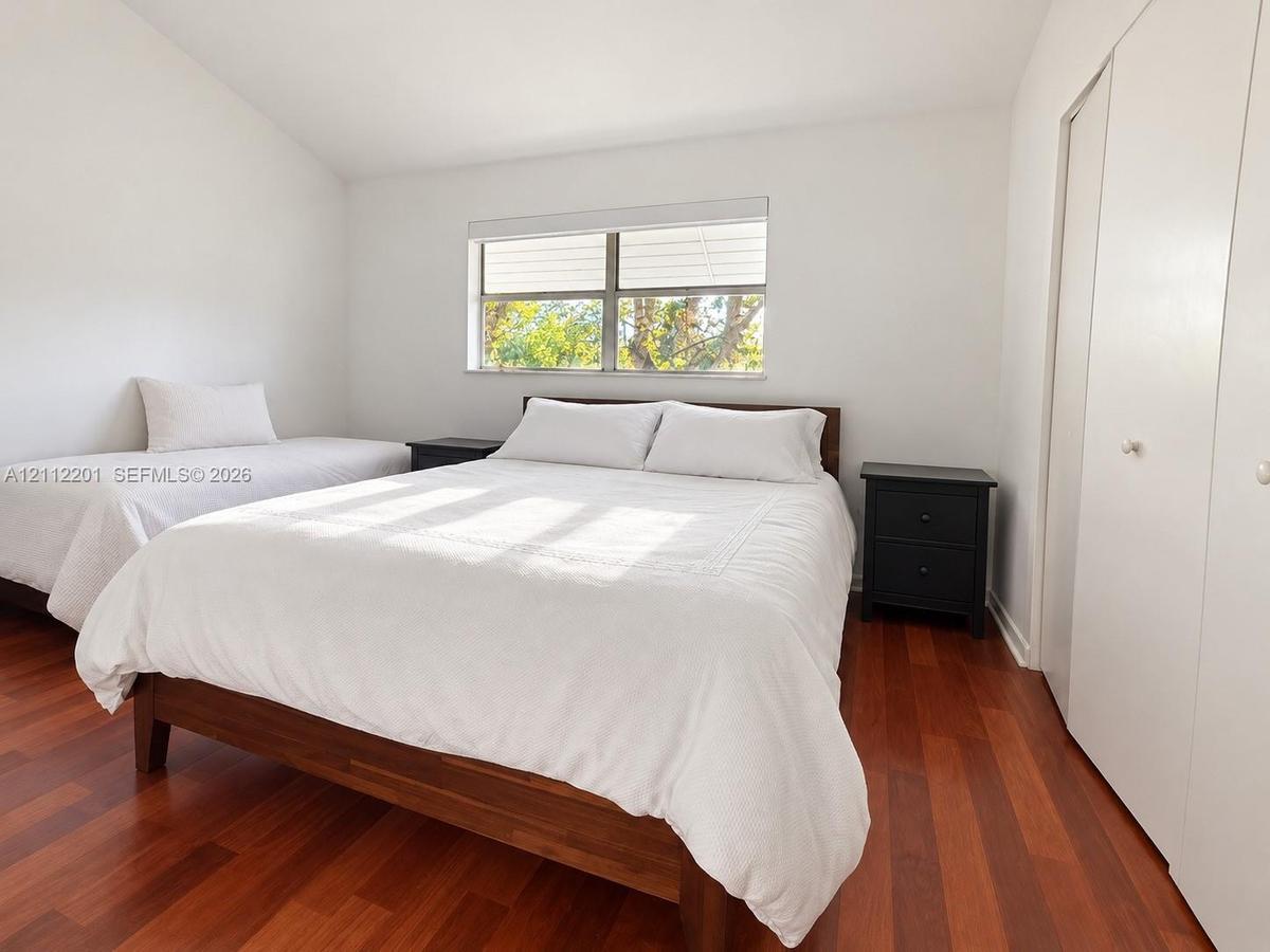 Vaulted ceiling, wood-finish flooring, horizontal window with white window shades, and built-in closet with double doors