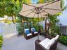 Private patio featuring grey tile flooring, solid perimeter walls, and a decorative white lattice gate surrounded by established landscaping