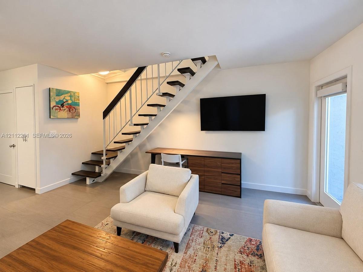 Open-tread staircase with dark wood-finish steps and white metal railings, large-format tile flooring, and full-glass panel door