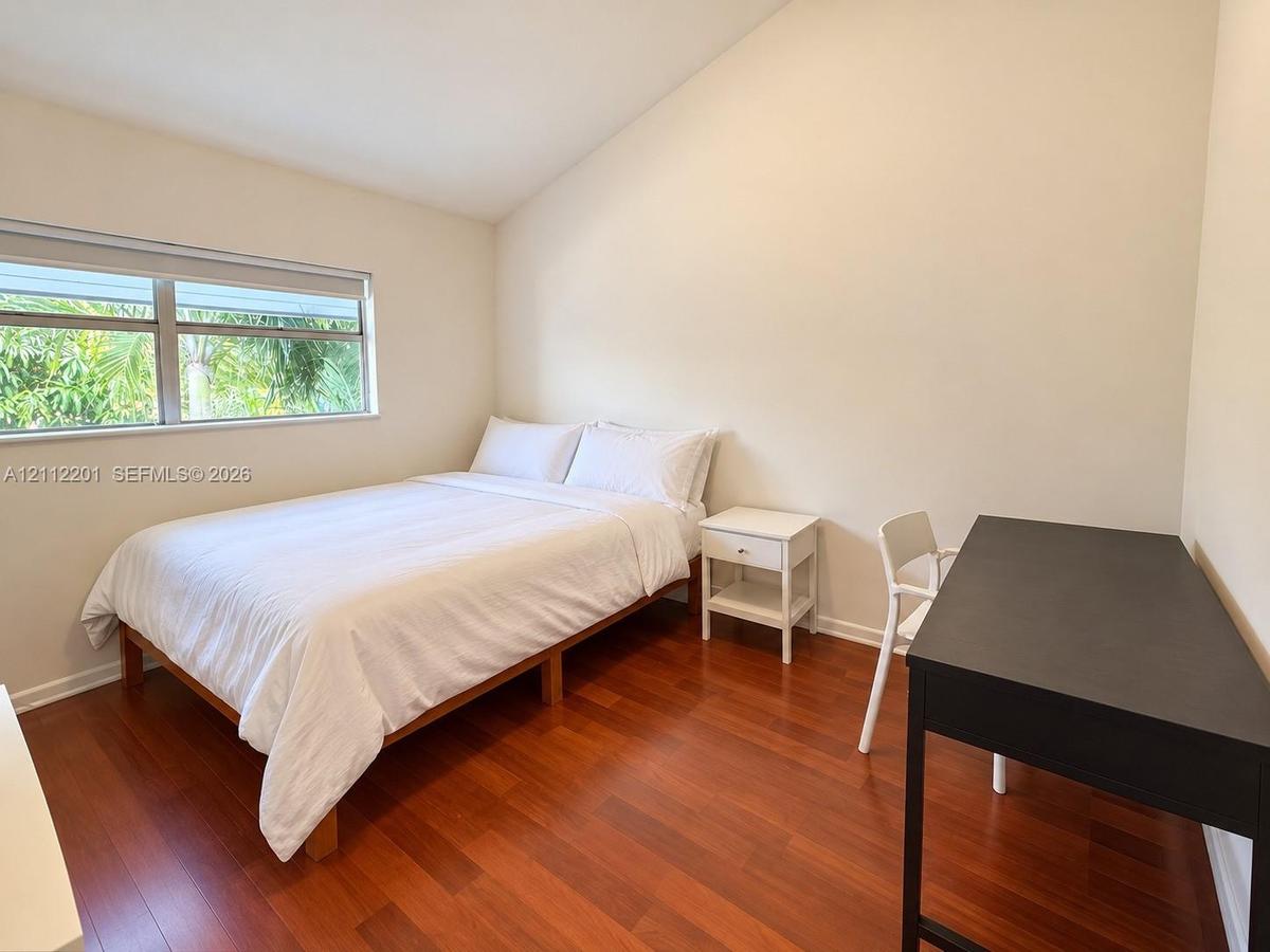 Bedroom featuring vaulted ceilings, wood-finish flooring, and a window with horizontal blinds