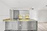 Kitchen featuring flat-panel wood-finish cabinetry, stone slab countertops, a waterfall-edge island with an integrated sink, under-cabinet lighting, a