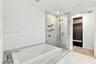 Soaking tub featuring stone-finish surround, glass-enclosed shower with rainfall showerhead, and built-in closet cabinetry