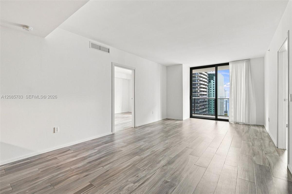 Open floor plan featuring wood-finish flooring, floor-to-ceiling glass sliding doors, and access to a balcony