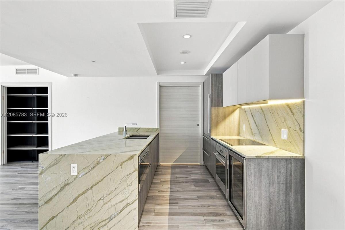 Kitchen featuring stone countertops with waterfall edge, wood-finish cabinetry, built-in stainless steel appliances, recessed ceiling lighting, and wo