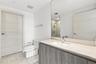 Bathroom featuring a vanity with stone countertop and integrated sink, full-width wall mirror, wood-finish cabinetry, two-piece toilet, and tile floor
