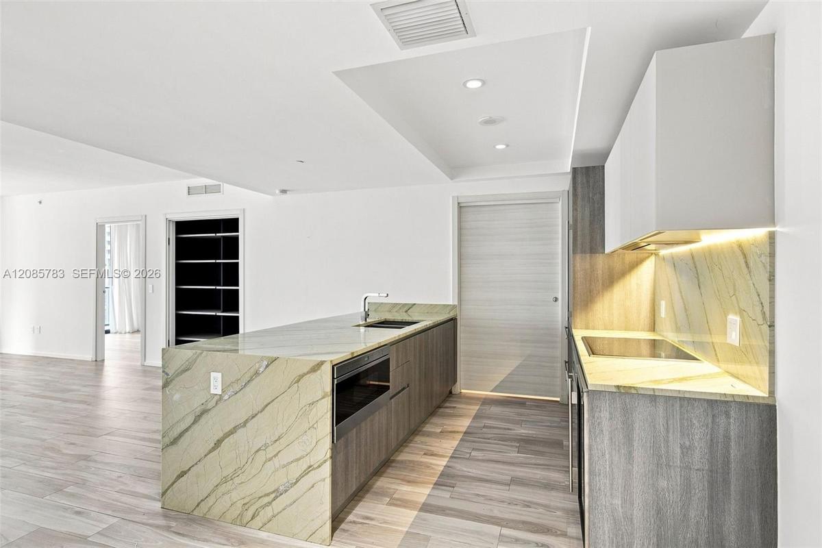 Kitchen featuring flat-panel cabinetry, stone countertops with matching full-height backsplash, waterfall-edge island with an integrated microwave, an