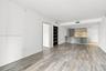 Open-concept interior featuring wood-finish flooring, a kitchen with stone-finish countertops and backsplash, dual-tone cabinetry, and built-in shelvi