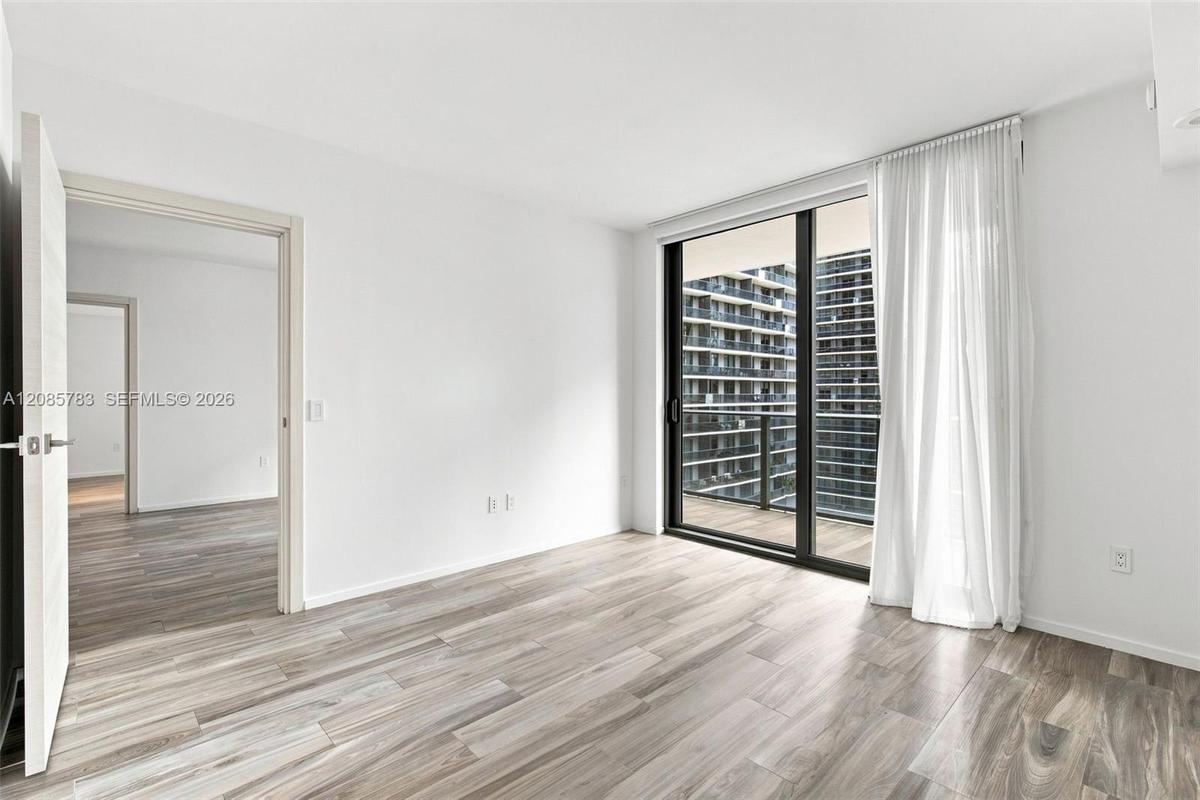 Wood-finish flooring, full-height sliding glass doors, private balcony, and neutral wall finishes