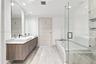 Floating wood-finish vanity with dual vessel sinks, stone-finish countertops, frameless glass shower enclosure, deep soaking tub, and stone-finish flo