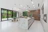 Kitchen featuring an oversized island with stone-finish waterfall countertop, wood-finish cabinetry, floor-to-ceiling glass sliding doors, integrated 