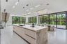 Kitchen featuring a large central island with waterfall-edge stone countertops, custom flat-panel cabinetry, matte black hardware, floor-to-ceiling mu