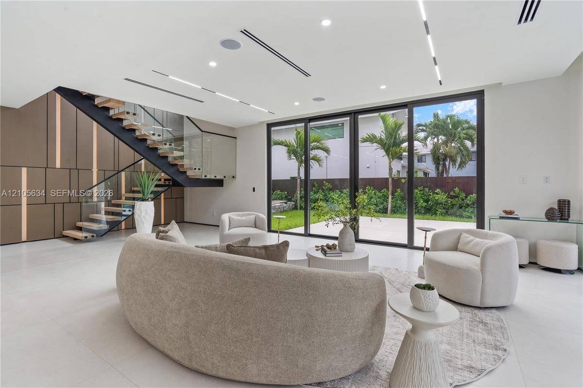 Open-concept interior featuring large-format tile flooring, a custom metal staircase with a glass railing, built-in decorative wall paneling, and floo