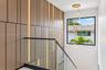 Custom wood-panelled accent wall with integrated vertical lighting, glass railing system featuring a black metal handrail, and multi-pendant brass cha