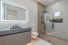 Floating vanity with integrated sink and matte black faucet, wall-mounted toilet, walk-in shower with glass enclosure, wood-finish tile shower wall, a
