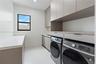 Laundry area featuring custom flat-panel cabinetry, light-toned stone-finish countertops, tile flooring, and integrated laundry appliances