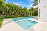 In-ground swimming pool with an integrated spa, featuring stone-style paver decking, decorative concrete stepping stones, and surrounding lush landsca