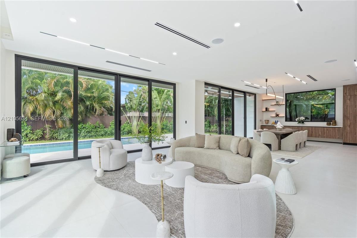 Open-concept interior featuring large-format flooring, expansive floor-to-ceiling sliding glass doors, recessed linear lighting, and built-in wood cab