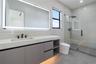 Floating vanity with integrated sink, stone-finish countertop, under-cabinet lighting, LED-backlit mirror, and glass-enclosed walk-in shower with matt