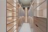 Walk-in wardrobe featuring custom cabinetry with wood-finish drawer fronts, open shelving, integrated vertical LED lighting, and matte black hardware