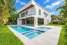 Modern two-story architectural exterior featuring smooth stucco finishes, floor-to-ceiling glass panel doors, a second-level glass-railed balcony, and